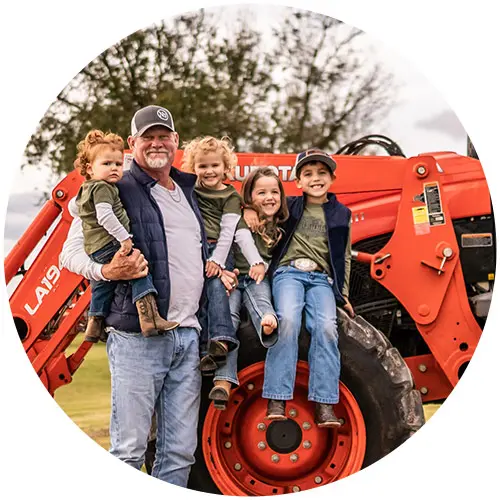 Family Farm Dairy famer with four children in front of a tractor in a field.